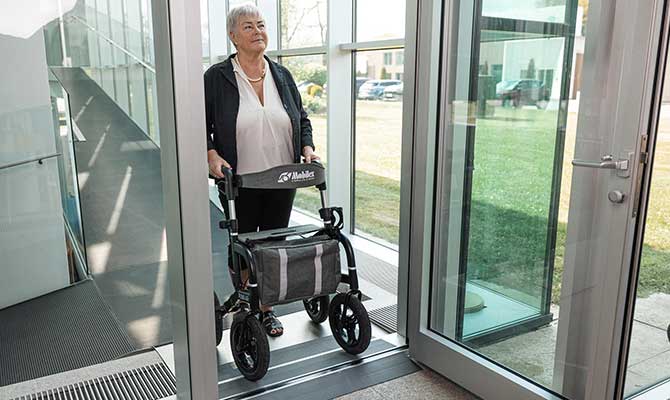 Kvinde i døråbning går over dørtrin med ramper med sin rollator